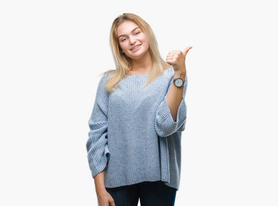 年轻的白种女人穿着冬季毛衣在孤立的背景做愉快的拇指手势与手。批准表达式看着相机显示成功