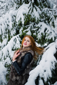 红头发的女孩穿着毛皮大衣在冬天下雪的公园散步