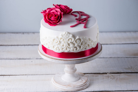 美丽的白色婚礼蛋糕装饰着鲜花红玫瑰和丝带。优雅假日甜点概念