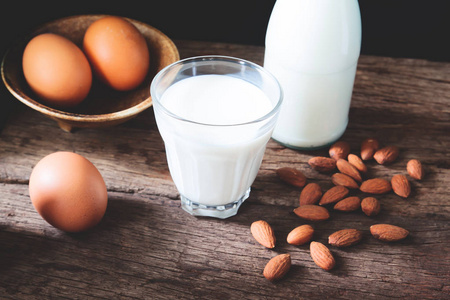 牛奶在饮料玻璃和瓶子用鸡蛋和杏仁在木桌, 健康食物