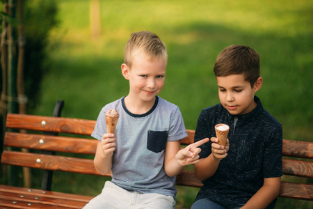 两个孩子在公园里玩耍。两个穿着 t恤衫和短裤的漂亮男孩笑得很开心。他们吃冰淇淋, 跳, 跑。夏天是晴天
