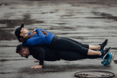 年轻的运动男人在雨中推着女人的体重