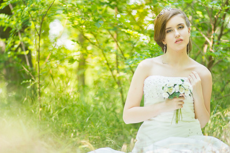 自然美丽的年轻新娘的画像。年轻女子在他们手中捧着一小束白玫瑰