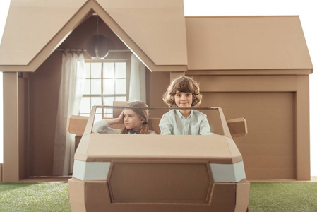 孩子们在房子前面坐着纸板车