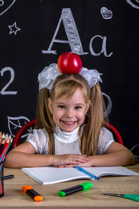 愉快和愉快的坏人女学生坐在书桌上的书籍, 学校用品, 与一个红苹果在她的头上