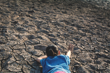 哀伤的女孩疲倦和用尽在破裂的干燥地面, 概念干旱和缺水危机
