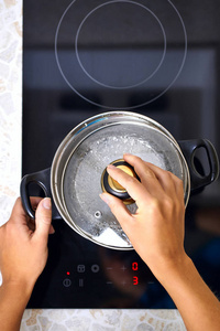 妇女手打开锅在现代厨房用感应灶