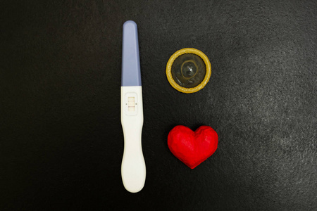 阳性妊娠试验和避孕套的木质背景, 两条和一颗红色的心