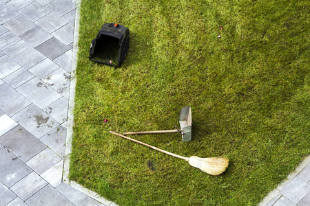 壶簸箕和一把扫帚在草地草坪上。园艺工具