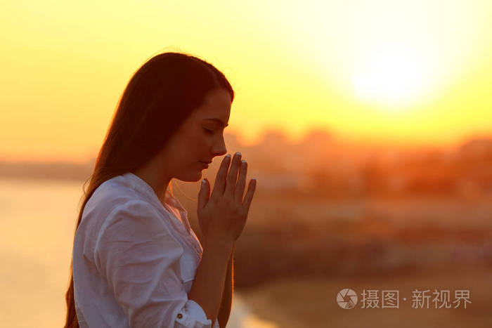 在夕阳下祈祷的女人的侧面视图