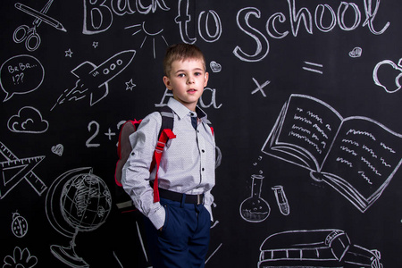 可爱的小学生站在黑板前, 背上背着背包。景观图片