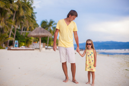 快乐的父亲与他可爱的女儿走在热带海滩度假