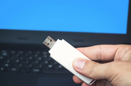 手握USB闪存驱动器在笔记本电脑背景。