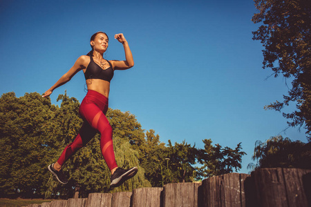 妇女在红色绑腿和体育顶部奔跑和跳跃在公园, 低角度看法
