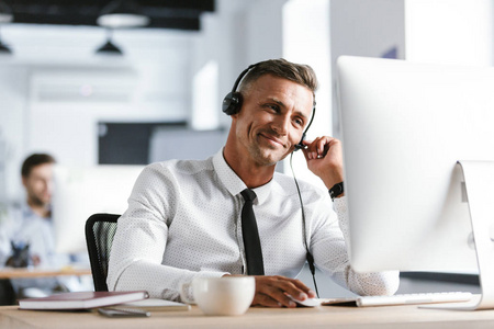 快乐操作员的相片30s 在呼叫中心的计算机上工作时身穿办公室衣服和耳机微笑