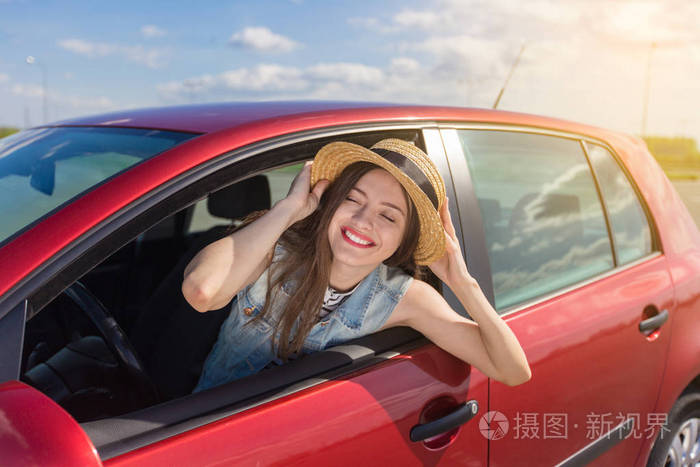 在车上的年轻女子.开车的女孩.微笑的年轻妇女坐在红色汽车