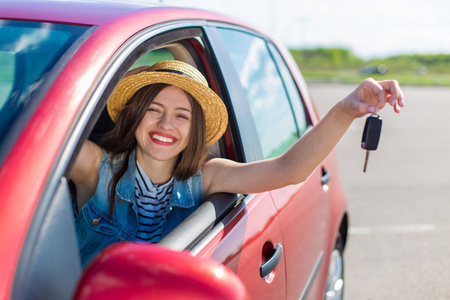 司机的女人微笑着显示新车钥匙和汽车。快乐的女人司机显示汽车钥匙和靠在车门上