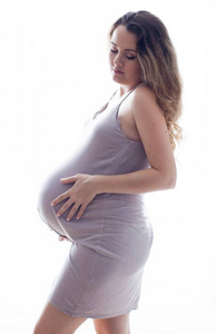 一个年轻漂亮的孕妇站在窗边。穿着漂亮的连衣裙怀孕了。母亲.怀孕.一个快乐的孕妇的肖像。舒适