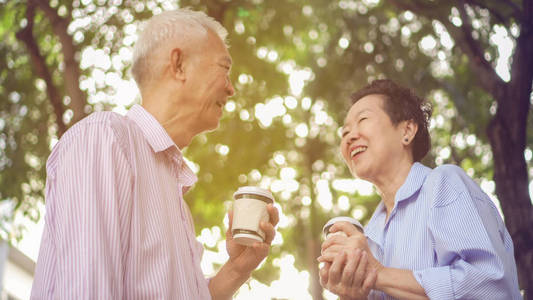 愉快的亚洲老人夫妇早晨散步在绿色城市喝咖啡和谈话