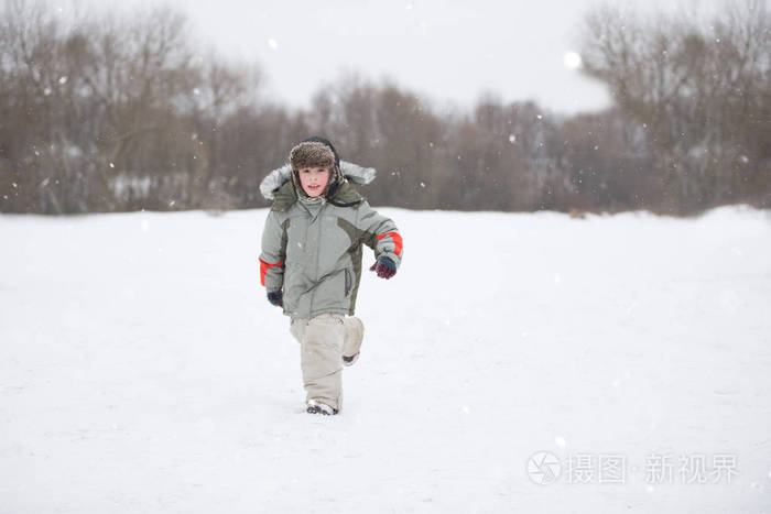 一个小男孩穿着暖和的衣服在雪地里奔跑帽子上戴着一顶毛皮帽子冬天的