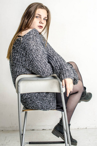 年轻漂亮的女孩坐在灰色的长厚的毛衣