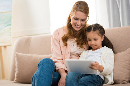 美丽微笑的母亲和女儿使用数字平板电脑一起在家里