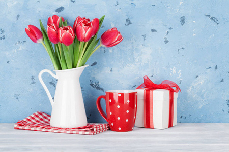 红色郁金香花束在水罐和礼物箱子。复活节或情人节贺卡。带空格的文本