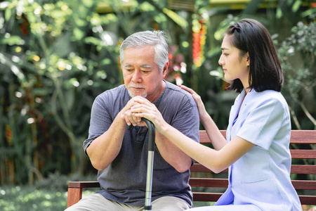 护士与病人坐在板凳上一起说话。亚裔老人和年轻女子坐在一起说话。严肃的心情