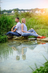 爱夫妇坐在岩石在河和日落看法