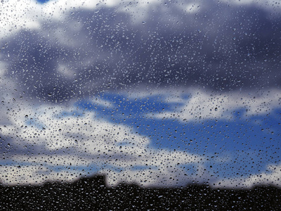 在蓝天下的窗户玻璃上的水滴与黑暗的雨云背景