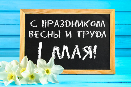 黑板与文本在俄语 与春天和劳动的假日, 5月1日。蓝色木桌上的水仙花白色花朵