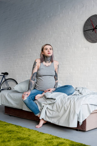 怀孕的纹身妇女坐在床上在家
