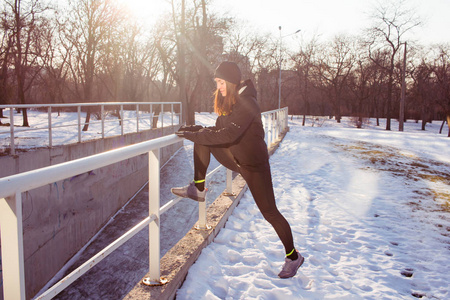 年轻女子运动员在黑色运动服奔跑在冬天公园