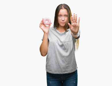 年轻的白种女人吃甜甜甜圈在孤立的背景与开放的手做停止标志与严肃和自信的表达, 防御手势