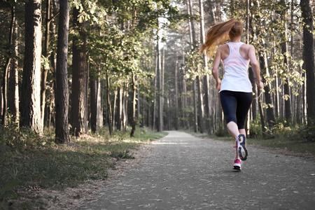年轻的白人红头发瘦女孩在森林里奔跑。晨跑。从后面查看