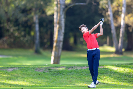 年轻的高尔夫球运动员击中球在竞争期间木材