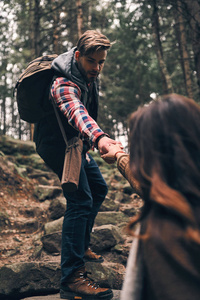 英俊的男子牵着手和移动他的女朋友, 而登山在山上的岩石楼梯