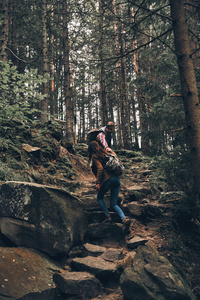 英俊的男子牵着手和移动他的女朋友, 而登山在山上的岩石楼梯