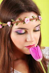 年轻漂亮的女孩在装饰花环与郁金香在她的手，在绿色背景上