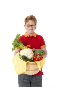 健康饮食。红色的头发和眼镜持有与新鲜蔬菜安排一篮子的白种人小男孩