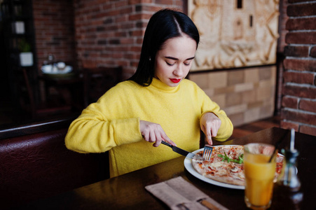黄色毛衣在餐馆吃比萨饼的滑稽黑发女孩
