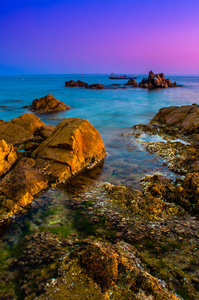 海浪在日落时撞击岩石。图像包含软焦点和蓝色由于慢快门