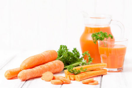 胡萝卜汁在美丽的眼镜, 切橙蔬菜和绿色欧芹的白色木质背景。鲜橙饮料。关闭摄影。选择性对焦。水平横幅