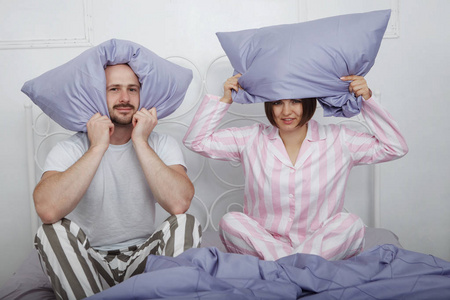 年轻的美女和一个秃头胡子男子在睡衣坐在他们的头上的枕头在床上的蓝色床上用品