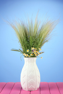 野生花卉和草药，在彩色背景上的木桌子上的花瓶中的花束