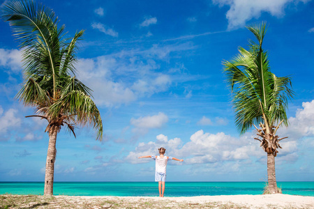 加勒比假期, 海滩上穿着白色连衣裙的可爱小女孩。可爱的婴儿站在瓜岛棕榈树之间