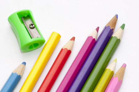鲜艳的彩色铅笔。彩色铅笔和削纸刀在白纸上