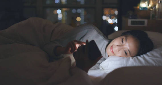 妇女发送手机短信和躺在床上