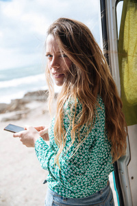 年轻的金发女郎与她的手机在一个美丽的大海前