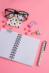 记事本, 钢笔和眼镜在粉红色的背景。平坦的。桌上的办公用品